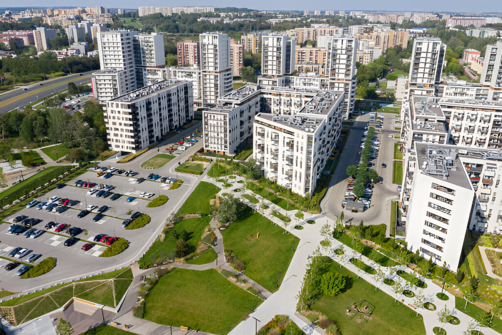 A 3D architectural rendering modern urban residential complex featuring multiple tall buildings surrounded by green spaces, walkways, and a parking lot, located in a bustling cityscape.